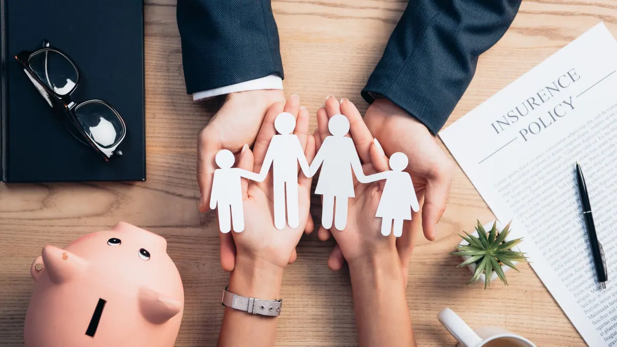 Unas manos junto a una hucha resguardan a una familia de papel, una imagen para la guía sobre cómo comparar seguros de decesos entre compañías