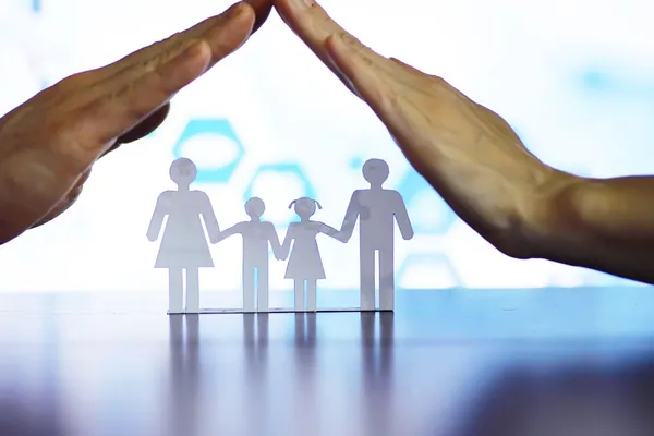 Seguro de decesos para extranjeros y residentes en España: unas manos que protegen la silueta de papel de una familia